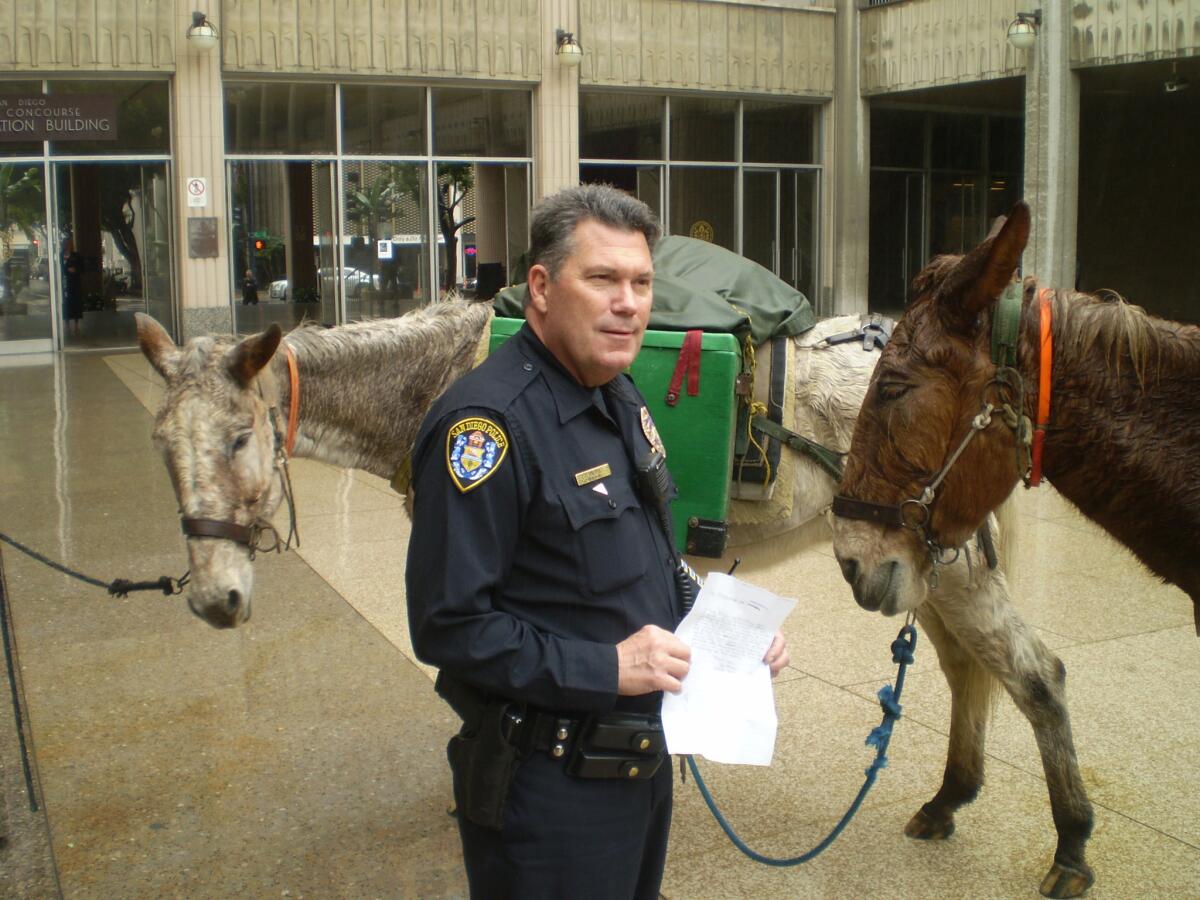 Police Officer Clinton Castle accepts an "emergency declaration" presented to him by John Sears and his two mules in the plaza at San Diego City Hall. The declaration asked city officials to build more mule trails.