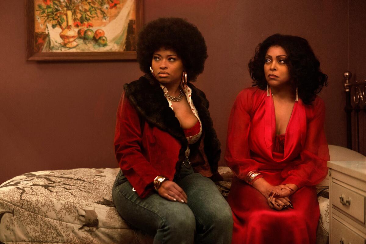 Two women are sitting on a bed next to a white nightstand.