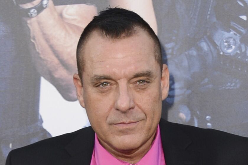 A man with short brown hair posing in a black suit and pink shirt