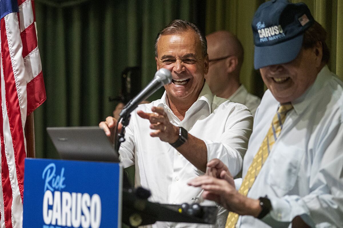 L.A. mayoral candidate Rick Caruso, left, reaching for a microphone at a lectern
