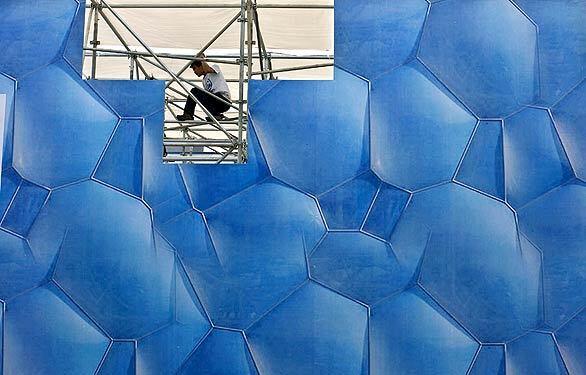 A worker climbs on scaffoldings while preparing a setup featuring the Water Cube, China's National Aquatic Center, for the 11th annual Beijing International High-Tech Expo. The expo opens to the public Wednesday and ends Sunday.