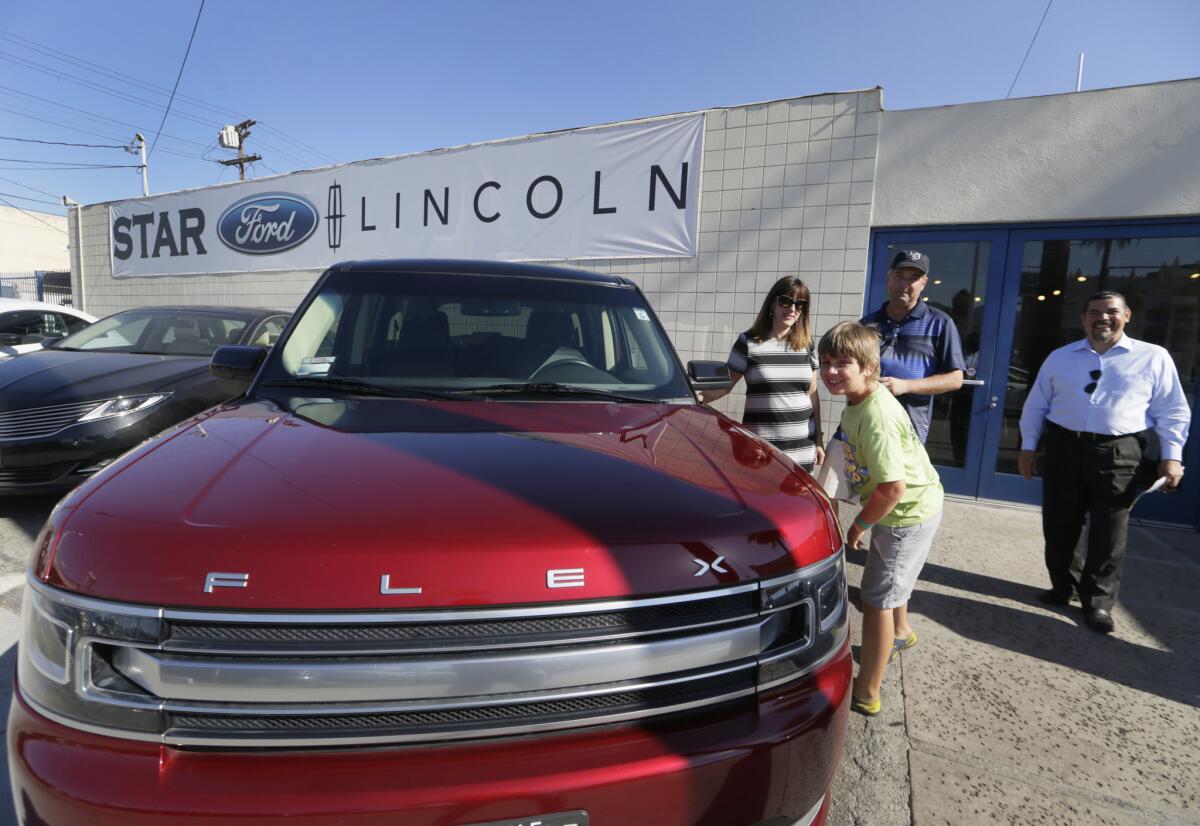 Robert Schemer, his wife, Kelly, and their son Graham, 9, pose next to their newly purchased pre-owned 2013 Ford Flex Limited, at the Star Ford Lincoln dealership in Glendale on July 2. At right is sales consultant Allan Calix.