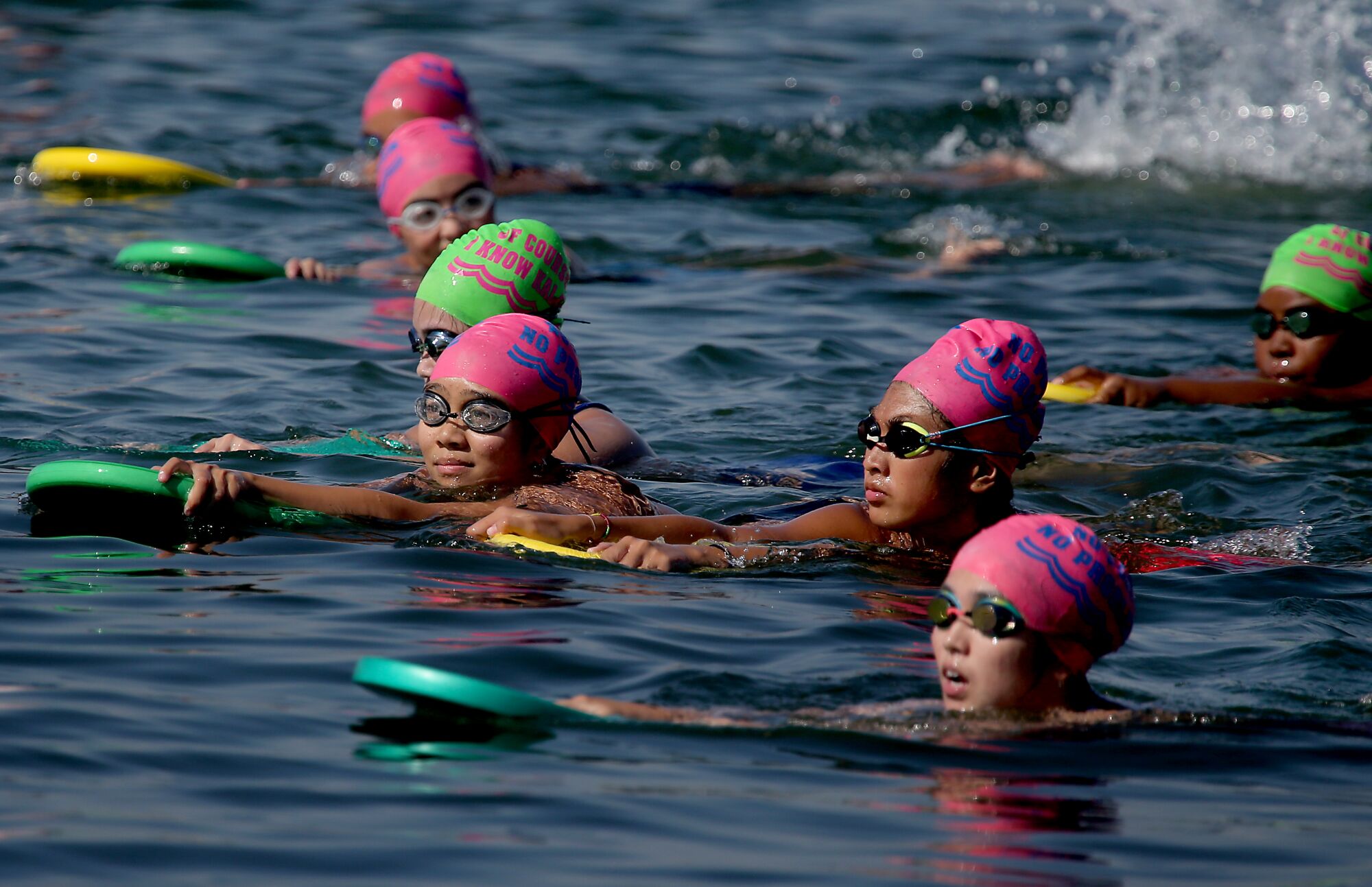 Swimmers in bright caps use kickboards