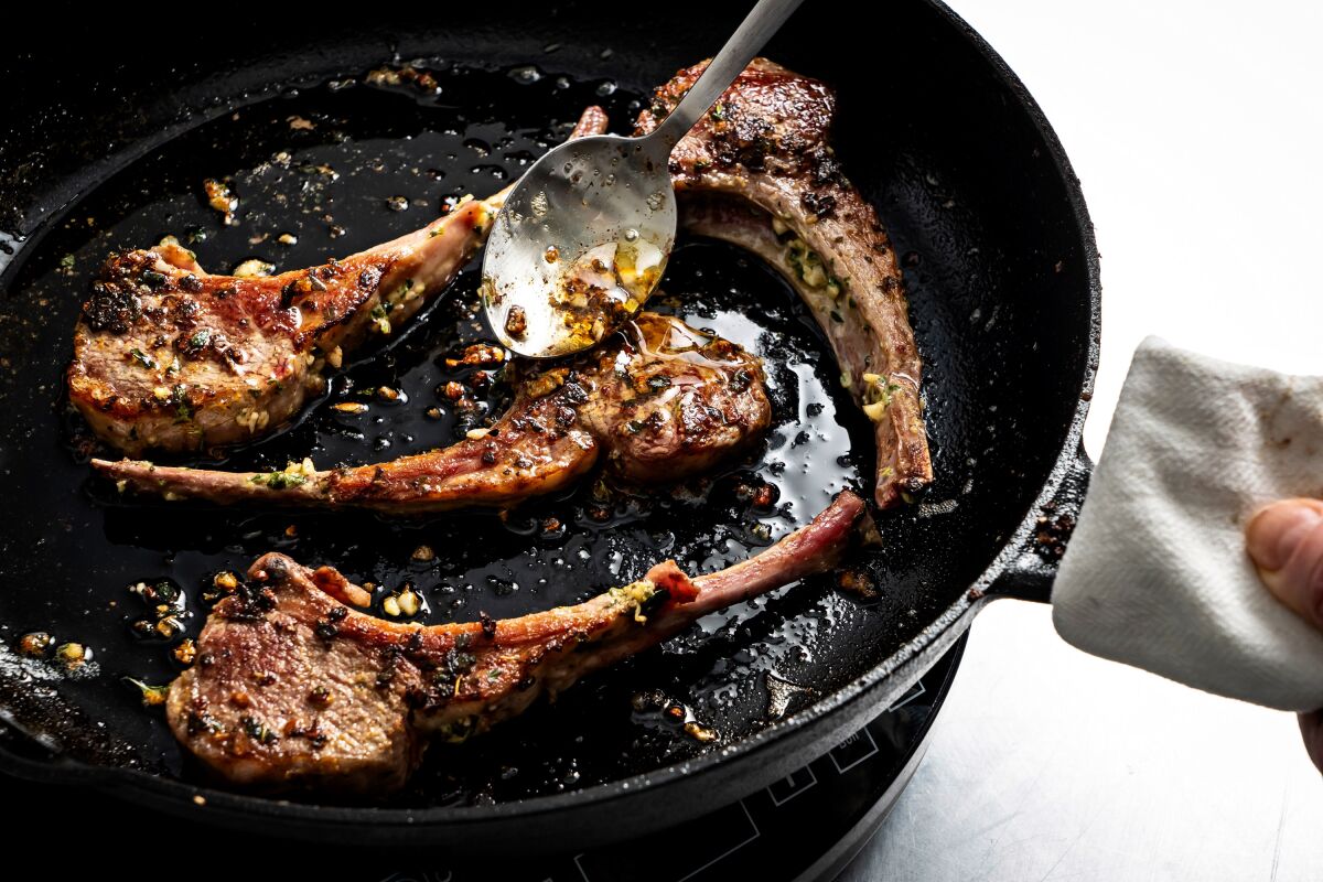 Butter and fat from the pan is spooned on top of lamb chops in a skillet.