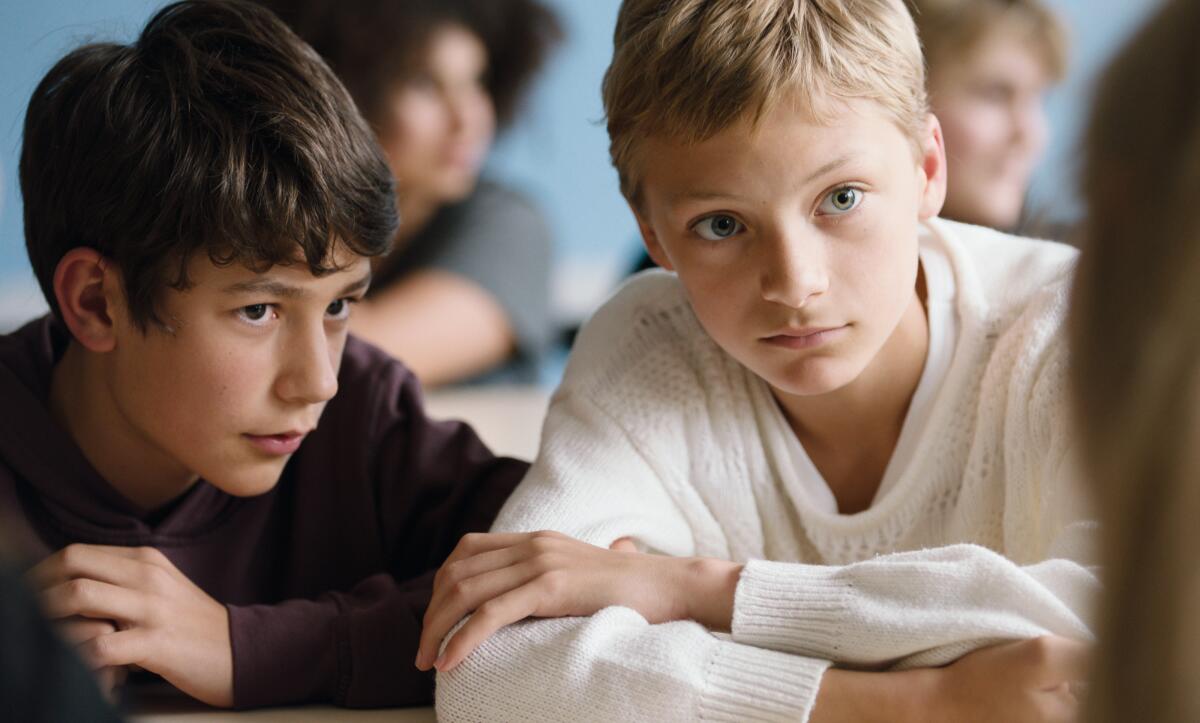 Two children, one in black, the other white, listen in a scene from the movie "Close."