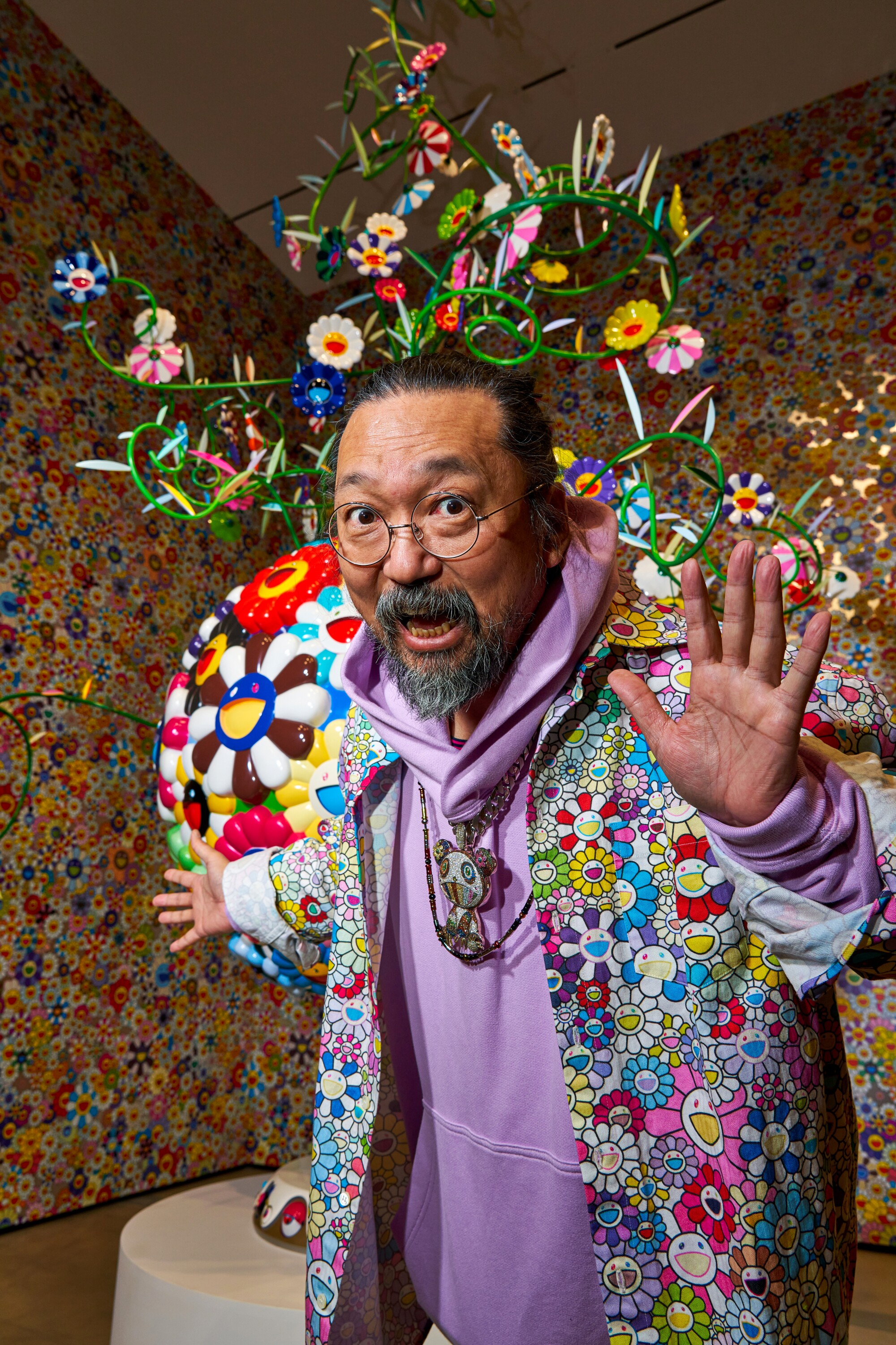A man in colorful clothing poses in front of an art sculpture.