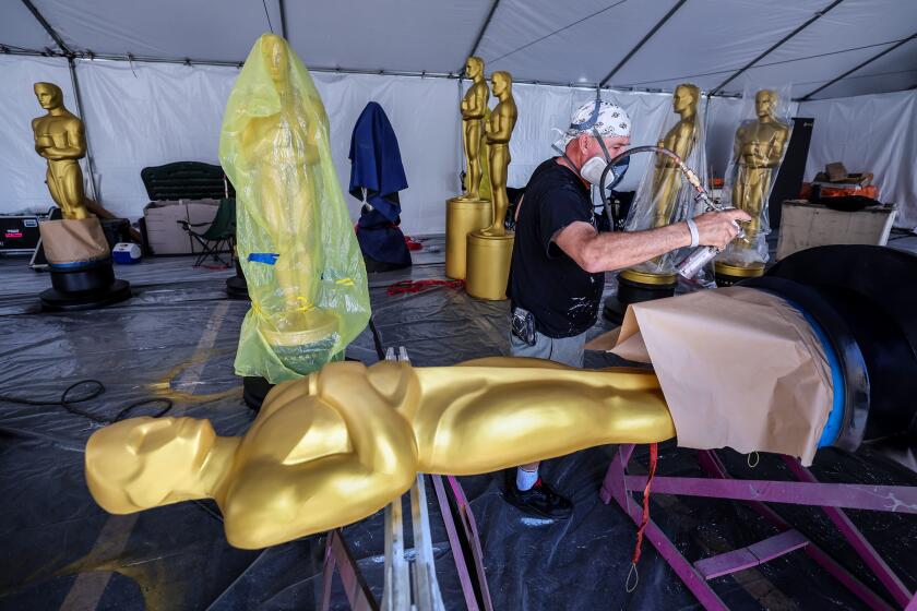 Los Angeles, CA, Friday, March 25 2022 - Assistant painter Rick Roberts applies the finishing touches on Oscar statues as construction continues on the red carpet of the 94th Academy Awards at Dolby Theater. (Robert Gauthier/Los Angeles Times)