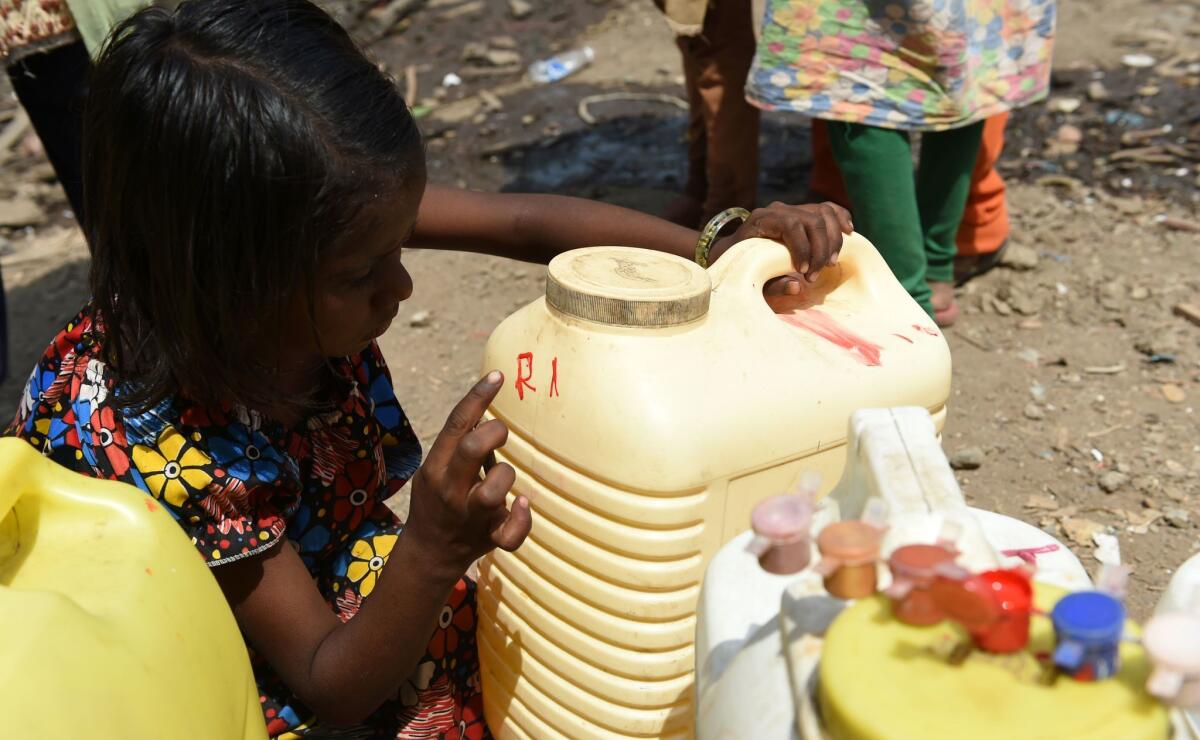 A child points to initials on a container on April 28 as she and other villagers line up to collect potable water at a makeshift camp in Mumbai.