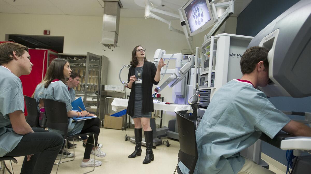 Christina Hwang, center, surgical education lab manager, goes over a da Vinci surgical robot as Corona del Mar High School Future Doctors Club member Zach Glabman, right, gets some hands-on experience with the machine at UCI Medical Center in Orange on Tuesday.