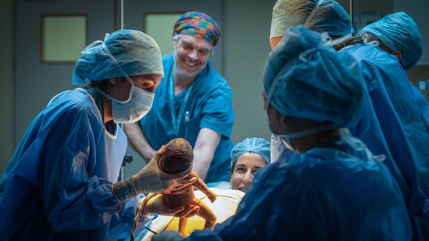 A doctor delivers a baby via c-section in a crowded operating room