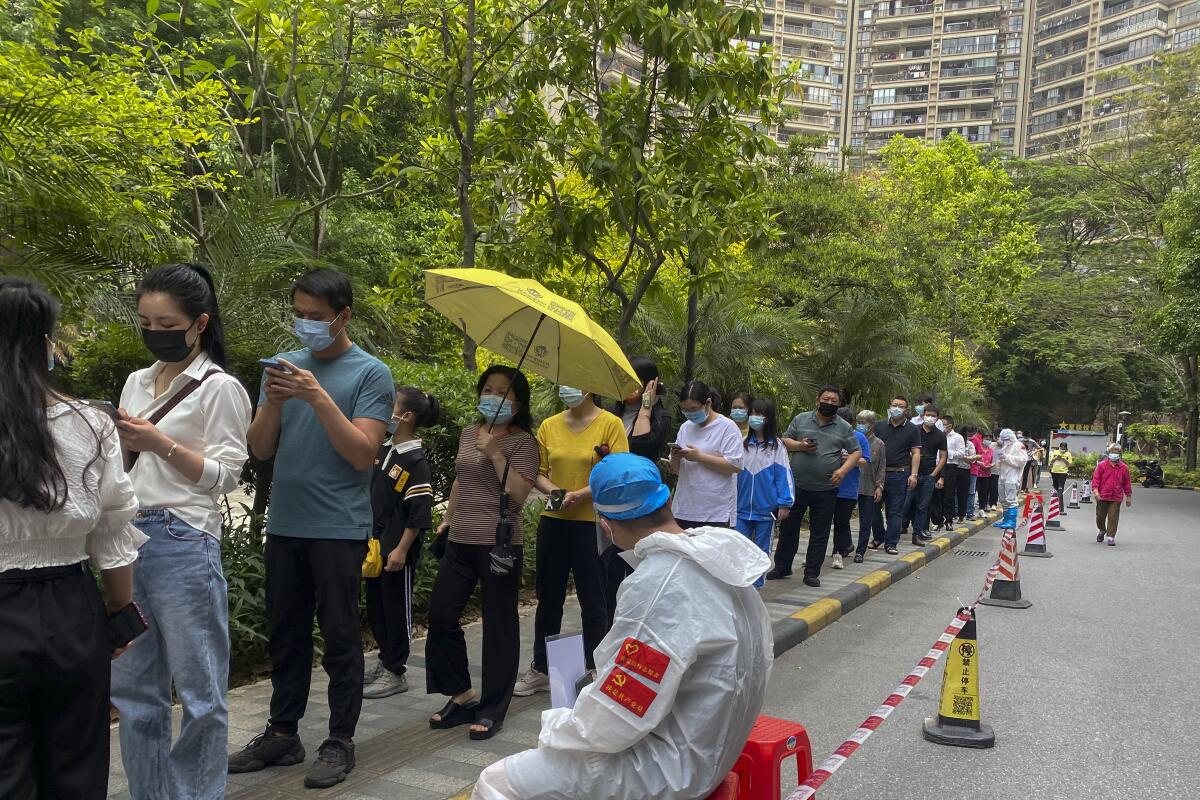 Workers in protective gear watch over residents lined up at a residential block in Guangzhou