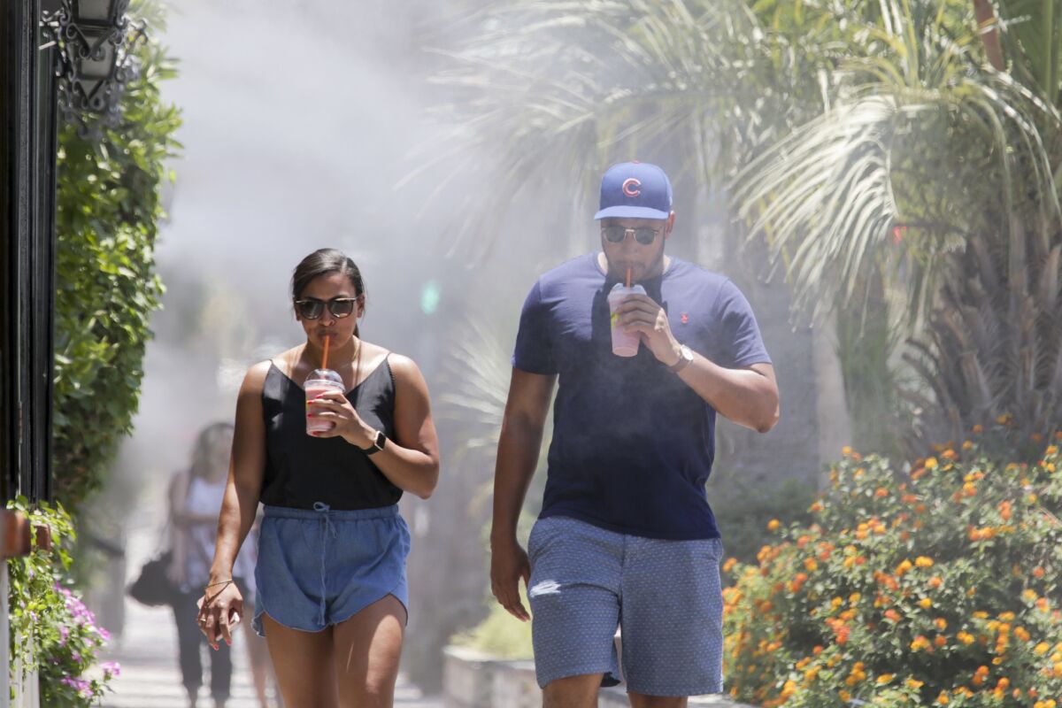Tina Robinson, left, and Eric Johns of Chicago beat the heat by walking under a cool mist and sipping colds drink in Palm Springs.