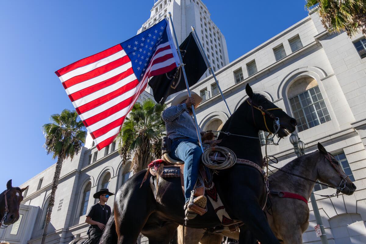  A man on a horse carries an American flag as others on horseback demonstrate outside City Hall