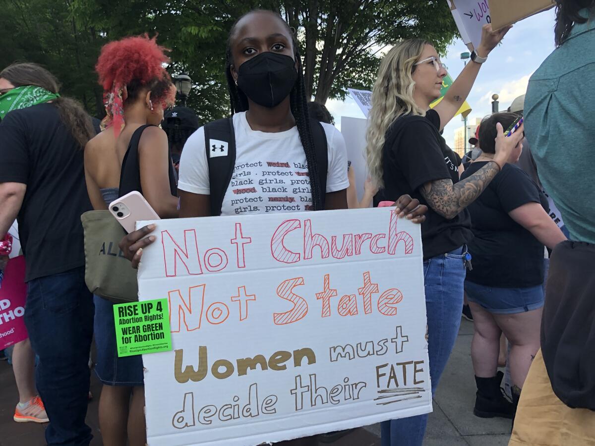 A young woman at a protest holds a homemade sign reading, "Not church. Not state. Women must decide their fate."