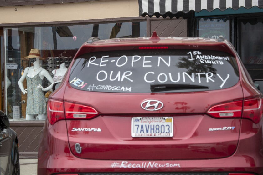 A motorist makes a statement on their car and a mannequin wears a protective mask in a store window display near the pier in Newport Beach on Tuesday.