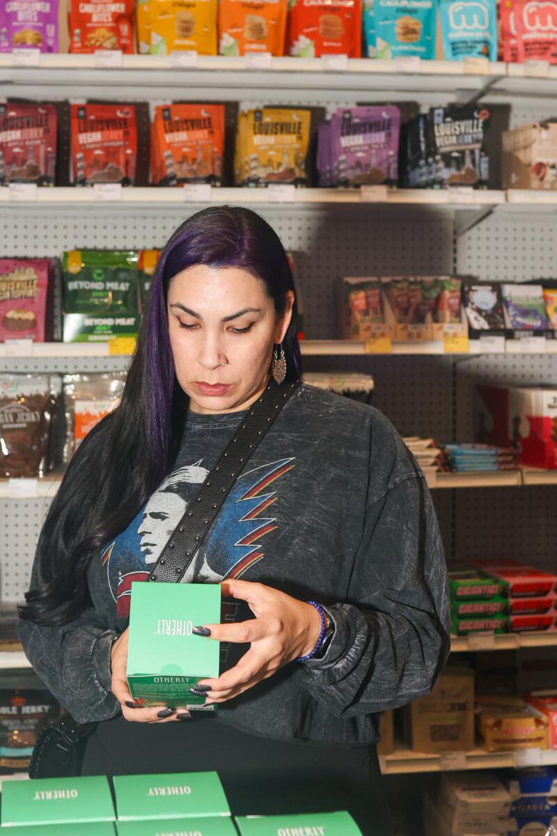 A woman looks at a product in a green box in a vegan grocery store.
