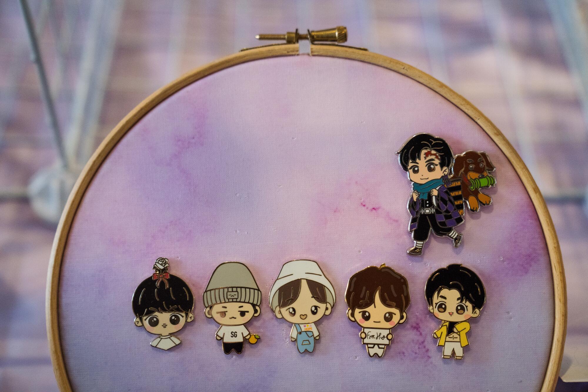 A needlework frame holds fabric on which are displayed pins depicting K-pop artists