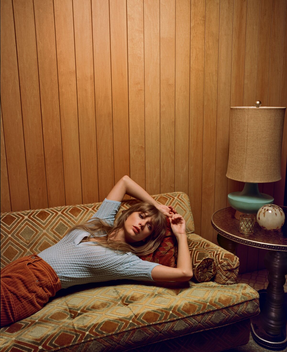 A woman reclines on a sofa in a wood-paneled room