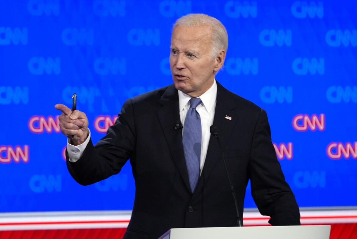 President Biden pointing to his right while standing against a blue backdrop with CNN logos repeated in red and light blue