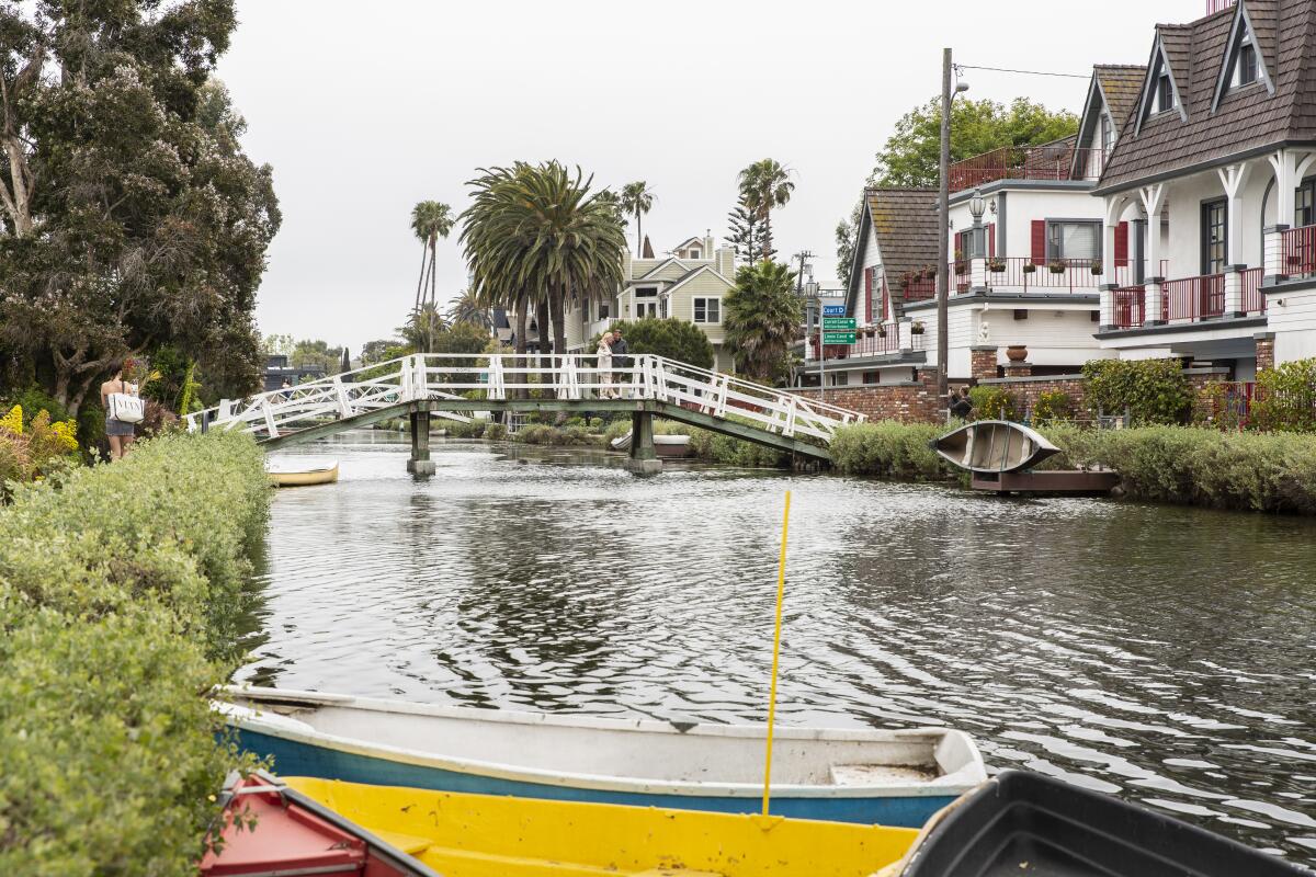 A bridge spans a narrow waterway that has colorful boats and is bordered by homes.