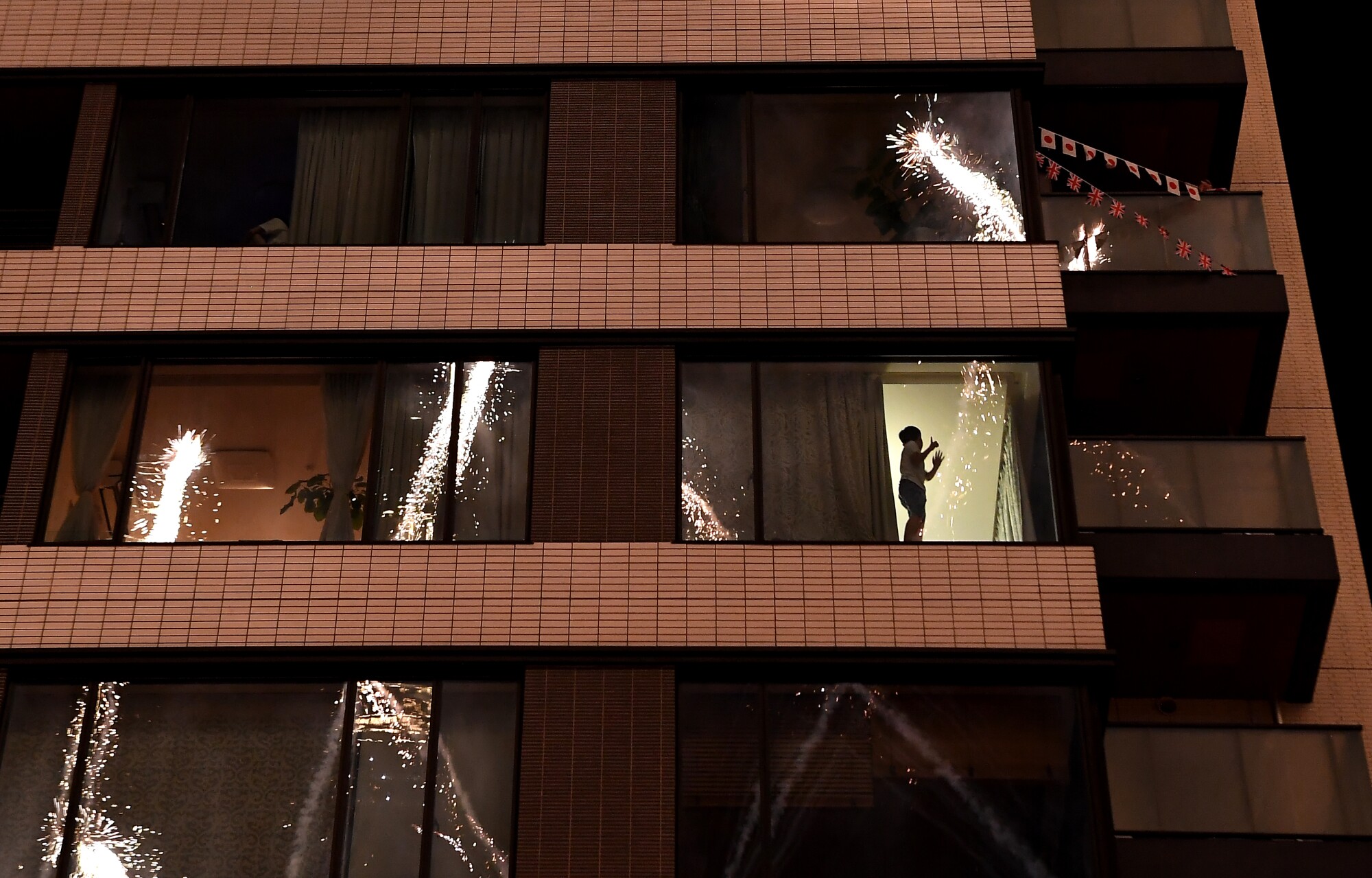 A young boy is seen in silhouette behind a window in a multistory building.