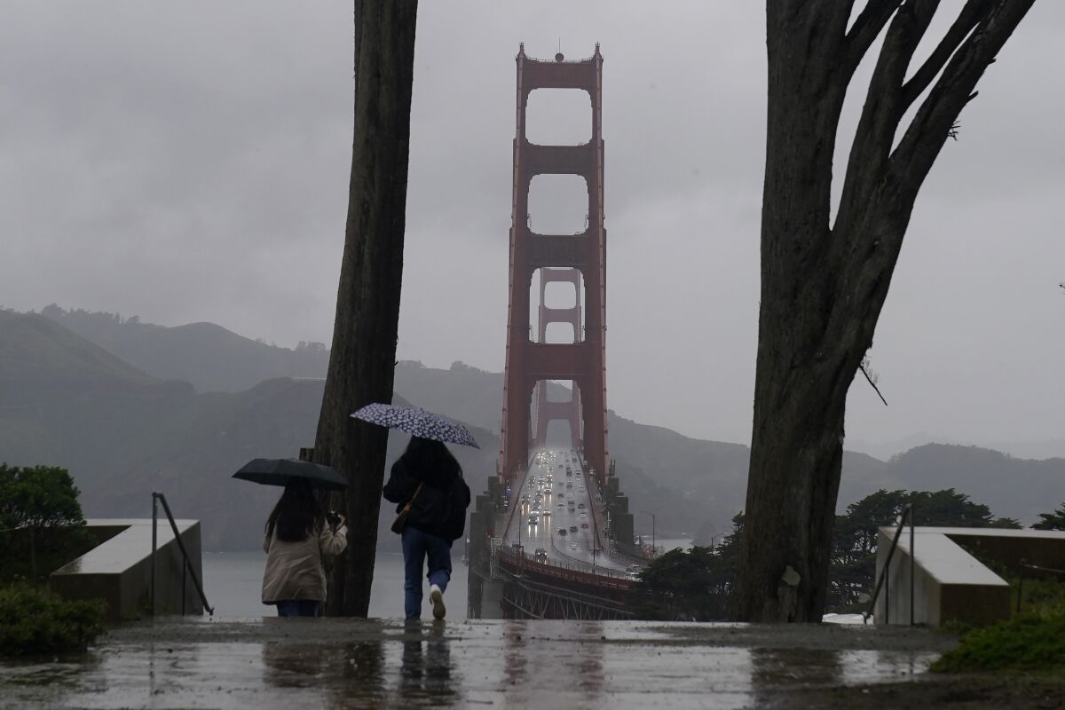 People carry umbrellas while walking down a path at the Golden Gate Overlook in San Francisco