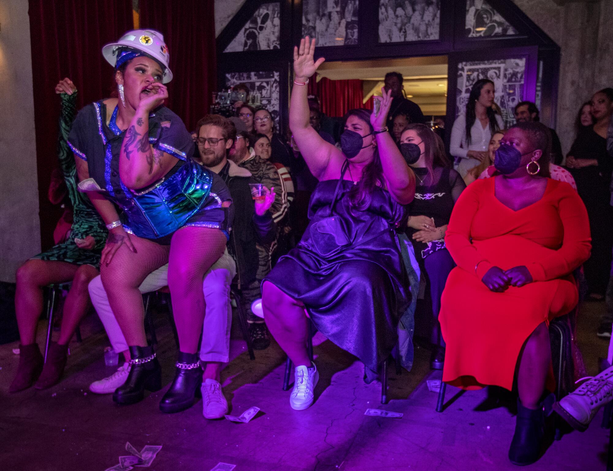 A burlesque dancer in a hard hat backs up to a cheering audience member.