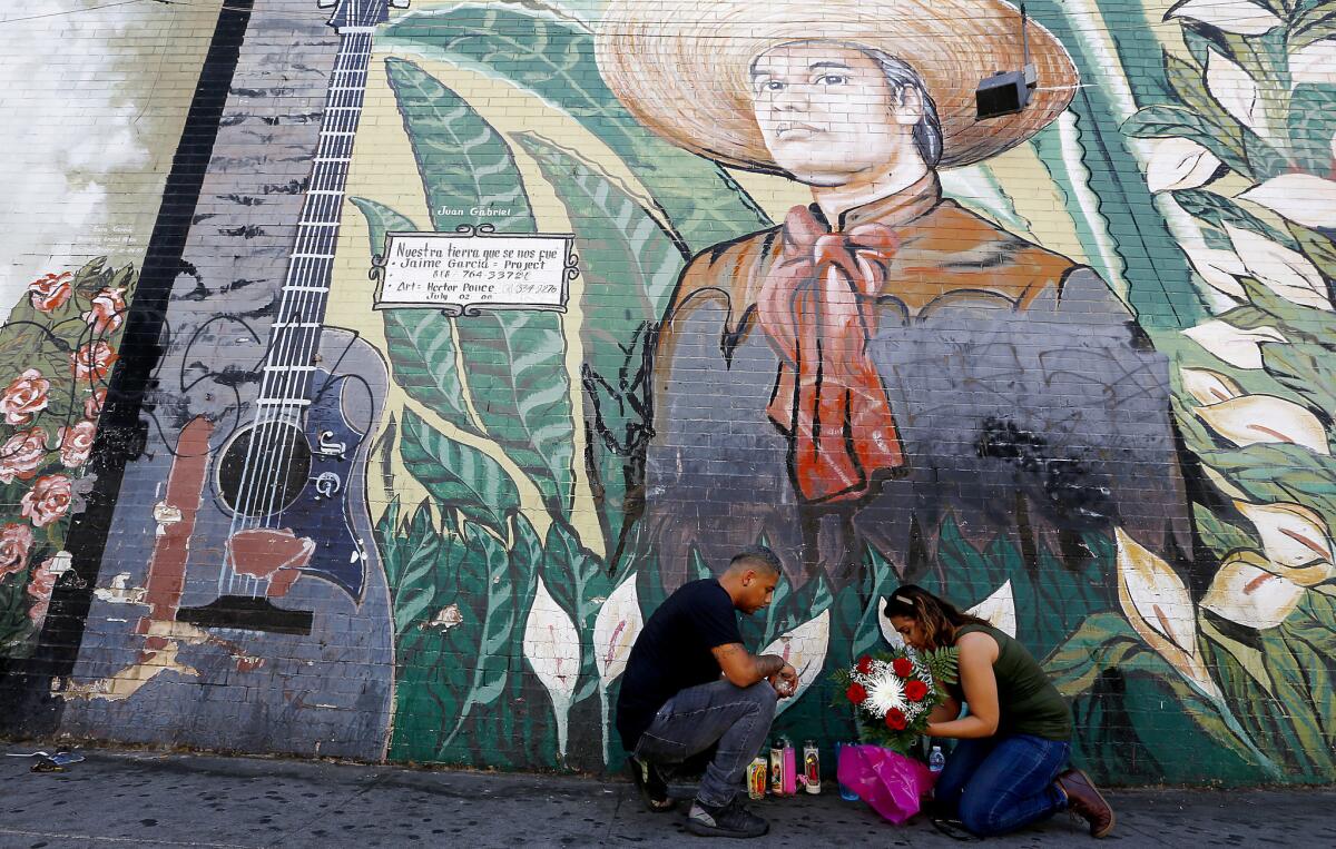 Los Angeles residents Javier Carrillo and Maria Galicia place flowers at the foot of a mural of Mexican singer-songwriter Juan Gabriel in MacArthur Park.