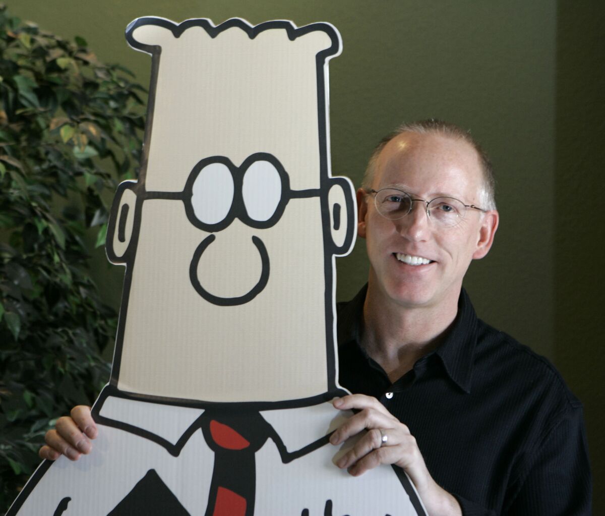 A balding man in glasses stands with his hands on the shoulders of a cutout cartoon character