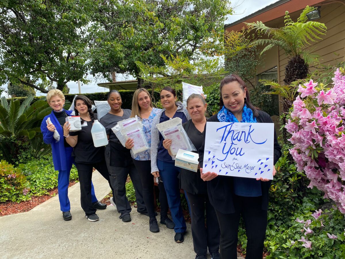 Dorothy Agustin, Sun and Sea Manor executive director, holds a "thank you" sign after the assited living facility received medical supplies from San Diego County. Behind her are the facility's staff and, at left, owner Anne Owens-Stone.