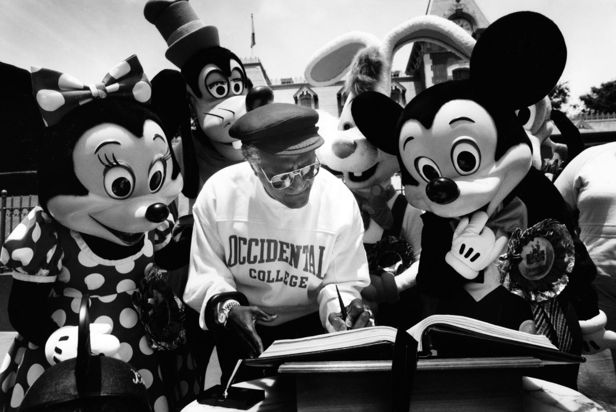 Archbishop Desmond Tutu, wearing an Occidental College sweatshirt, stands between Minnie and Mickey Mouse.