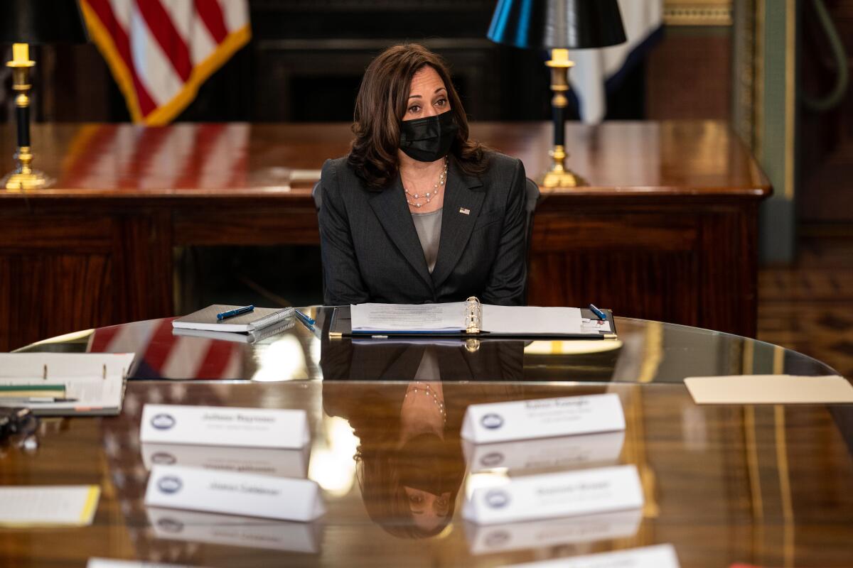 Vice President Kamala Harris wears a face mask sitting at a big table.