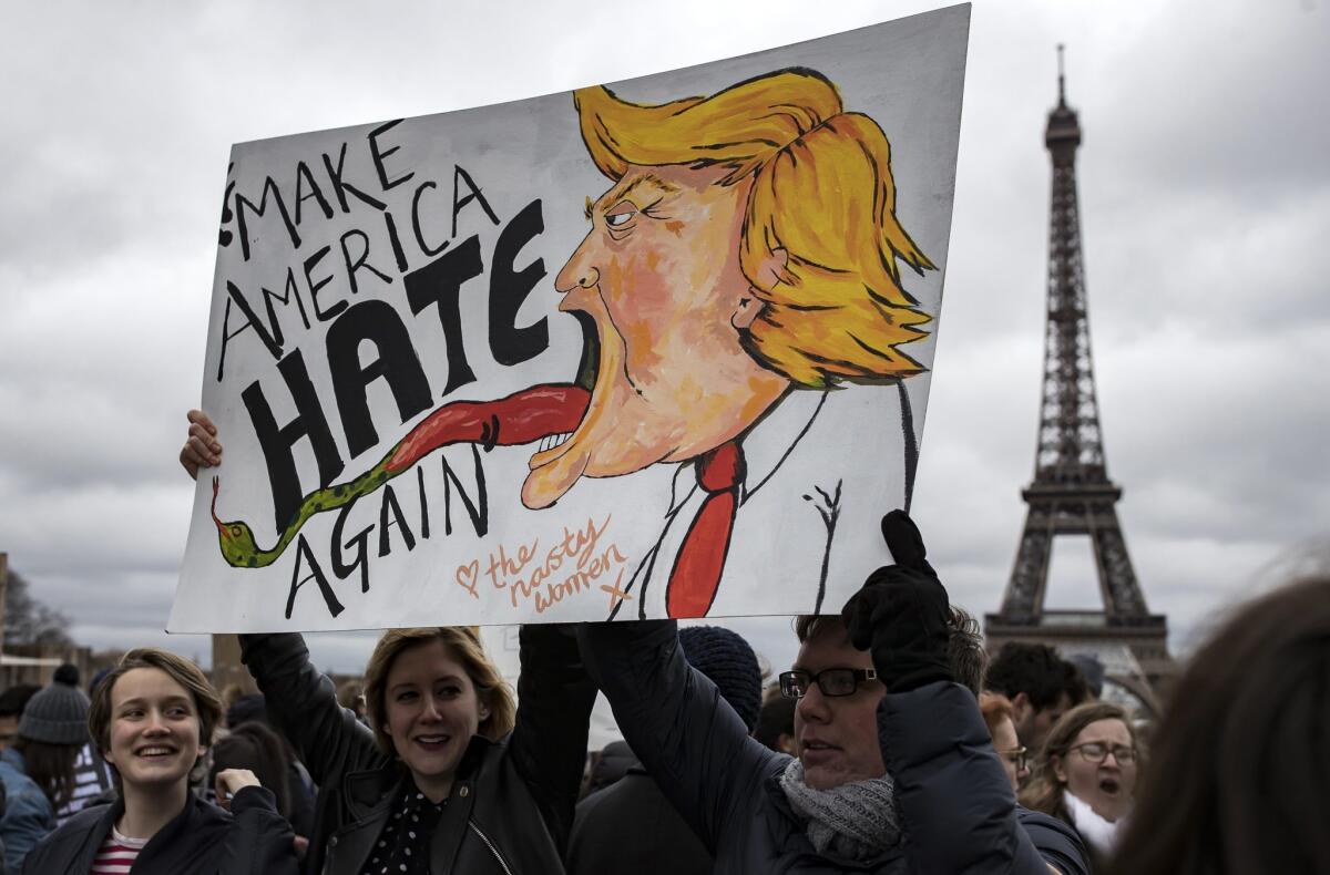 Protesters in front of the Eiffel Tower hold a sign with a caricature of a snake-tongued Trump saying Make America Hate Again