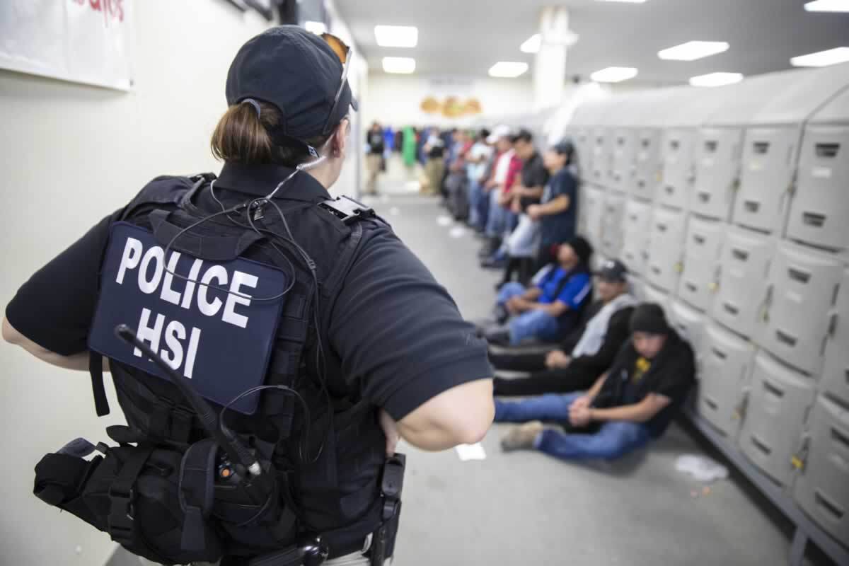 This image released by the U.S. Immigration and Customs Enforcement shows a Homeland Security Investigations officer guarding people picked up in an immigration raid Wednesday.