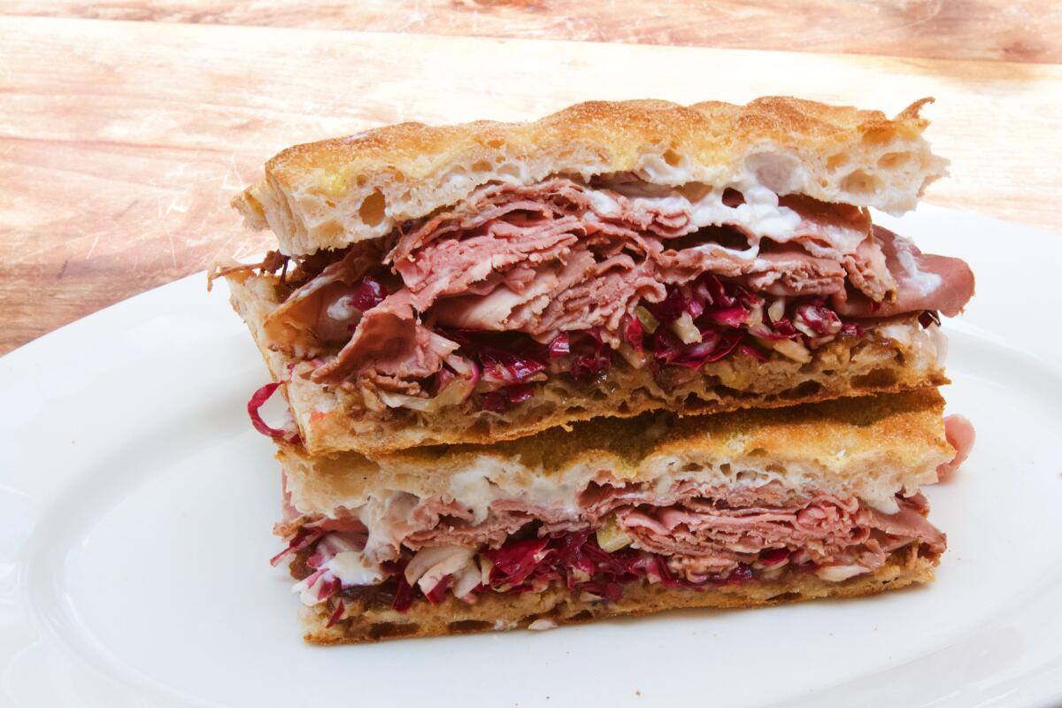 Two stacked halves of a roast beef sandwich with radicchio and horseradish cream on a white plate 