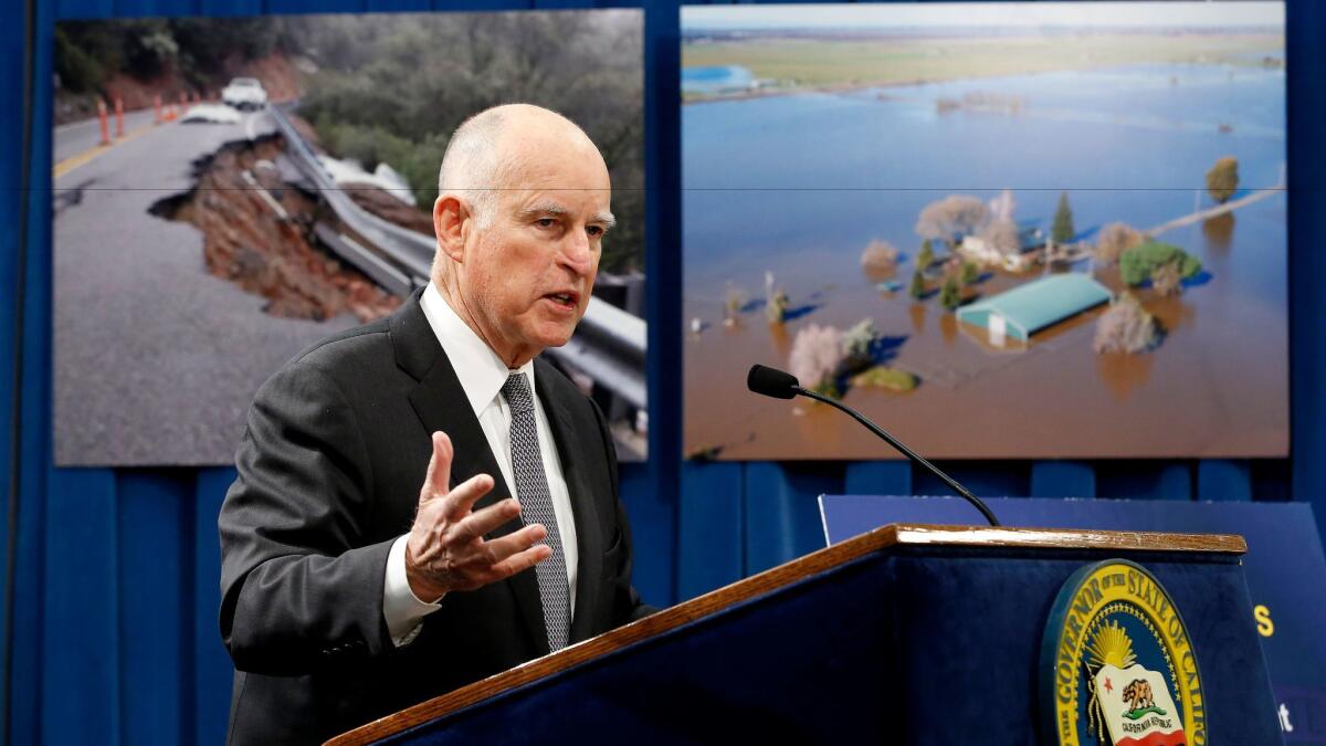 Gov. Jerry Brown discusses his proposal to spend $437 million on flood control and emergency response in the wake of recent storms, during a news conference Friday in Sacramento. In the background are photographs of recent storm damage.