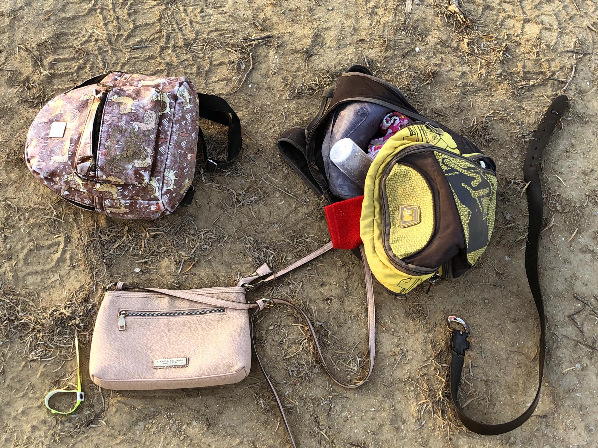 Backpacks, purses and a belt lying in the dirt