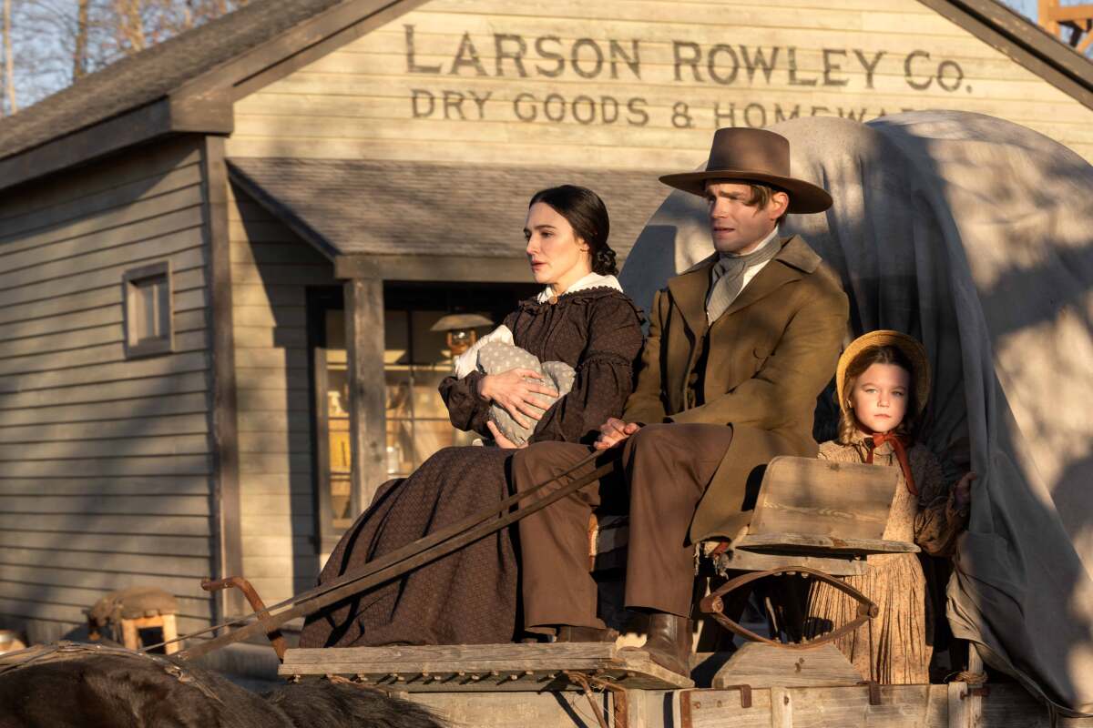 A 19th century couple driving a covered wagon with their two children.