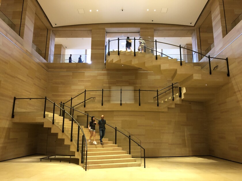 A view of a broad sandstone colored staircase that descends in a dramatic zig zag geometry