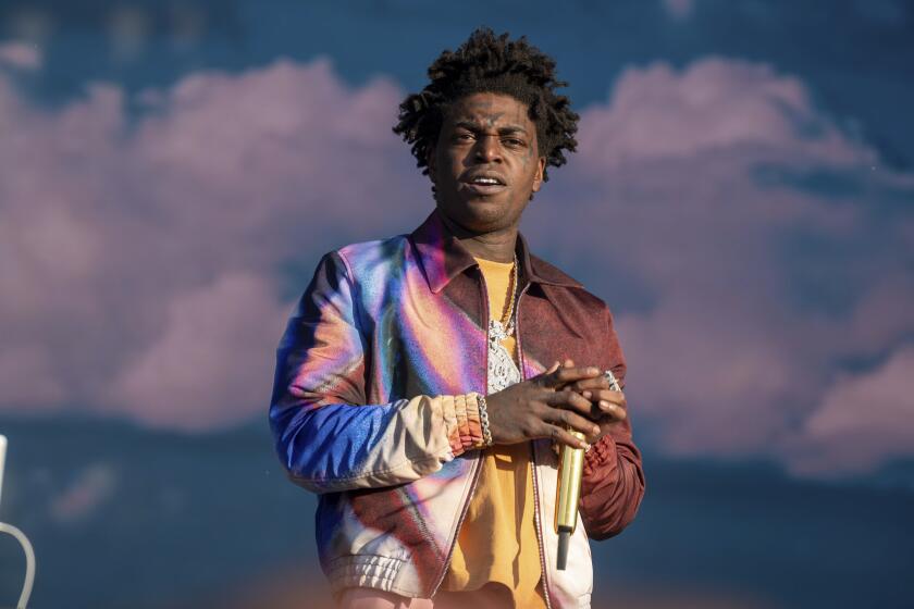 Kodak Black scowls while wearing a colorful bomber jack and holding a golden microphone 