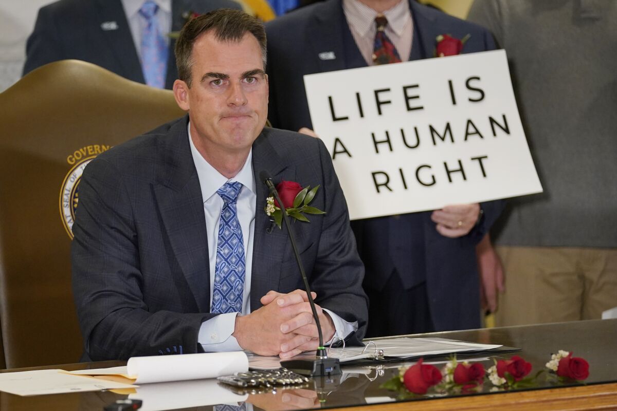 Oklahoma Gov. Kevin Stitt sits at a desk with a sign behind him that reads 'Life is a human right.'