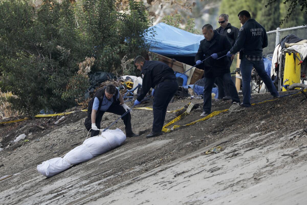 Coroner's investigators and police remove a body of homeless person who was shot to death at an encampment along the Arroyo Seco Parkway near Monterey Hills in 2018.