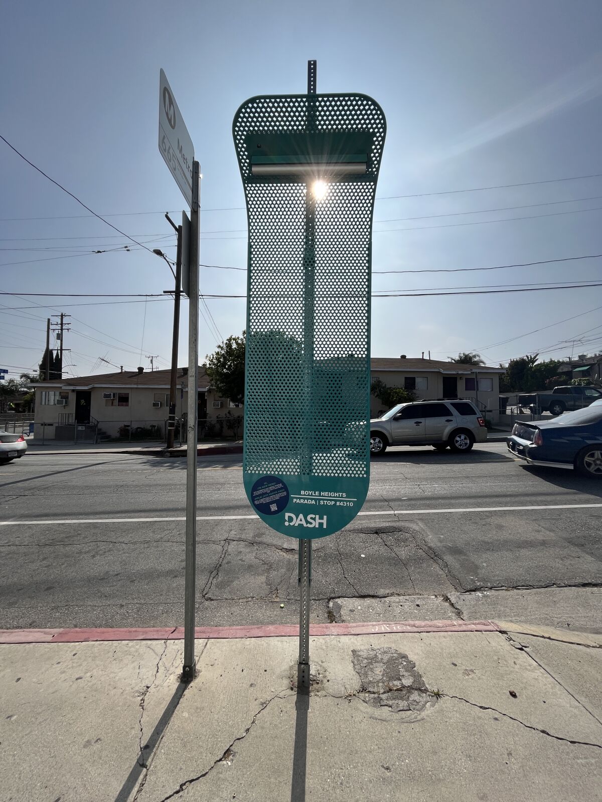 A piece of perforated metal attached to a street pole blocks the sun from view on a sunny Los Angeles street