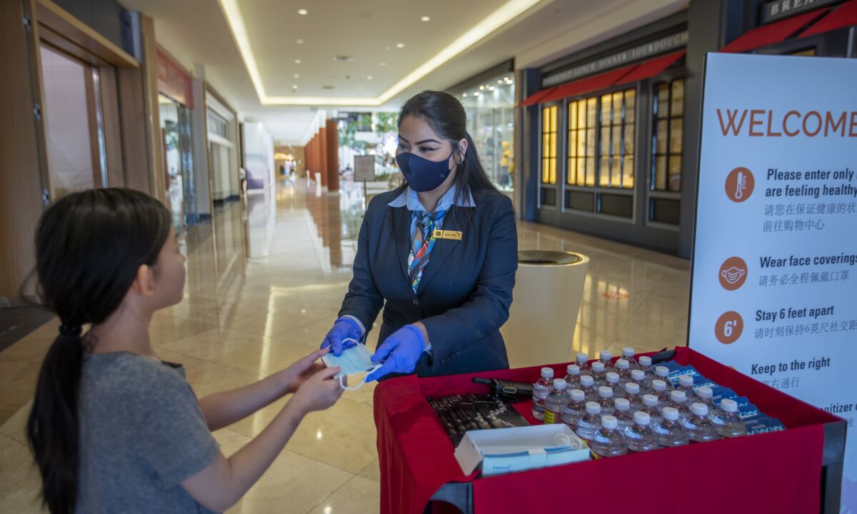 Mayra Trejo gives shopper Ada Gao a mask Thursday at South Coast Plaza in Costa Mesa.