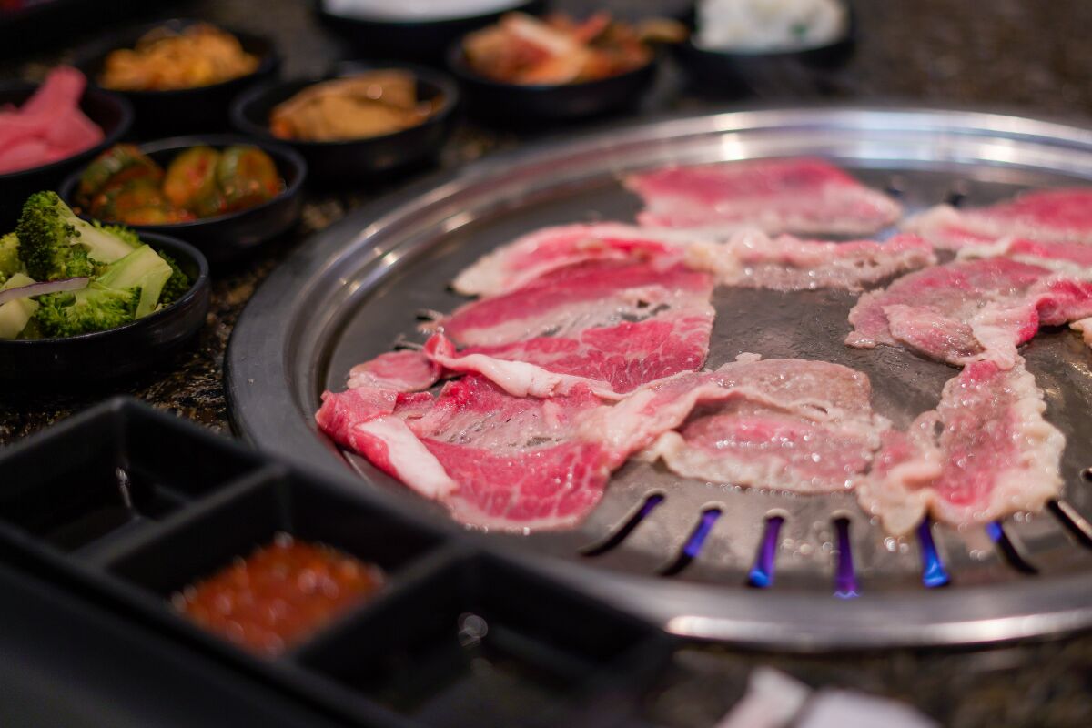 Thin slices of meat cooking on a tabletop grill.