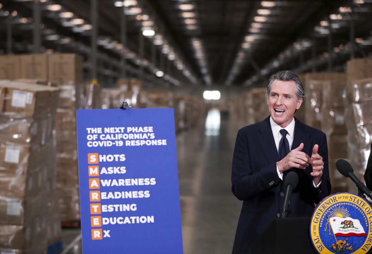 Gov. Gavin Newsom speaks at a lectern in a warehouse standing beside a poster propped on an easel