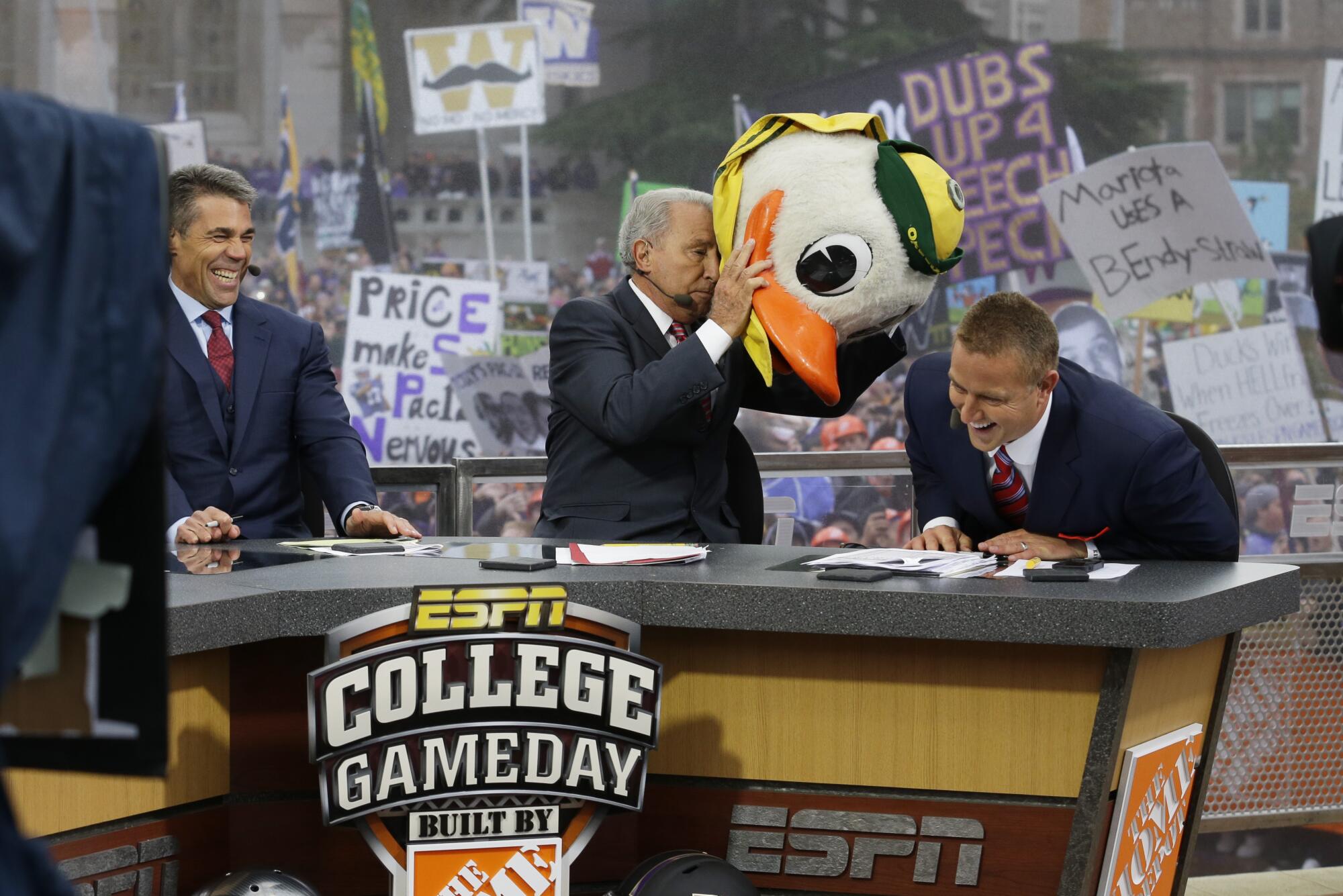 ESPN College GameDay host Lee Corso puts on Oregon Ducks' mascot head while Kirk Herbstreit and Chris Fowler laugh