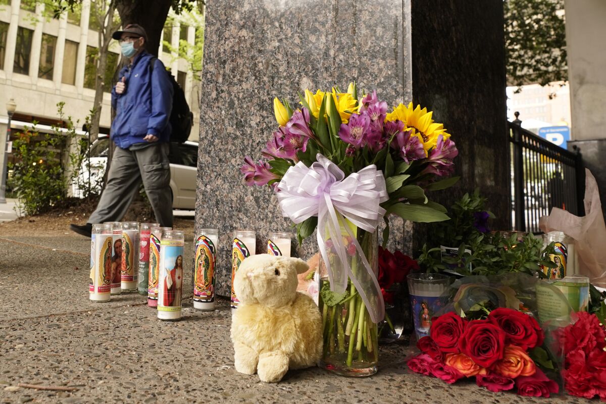 A person walking past a sidewalk memorial of flowers, candles and a stuffed animal