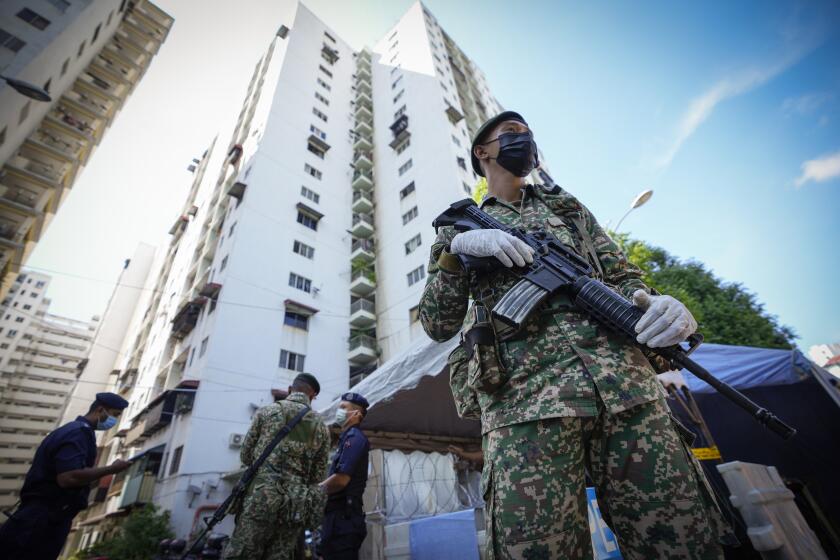 Armed soldiers stand guard outside Pangsapuri Permai, residential area placed under the enhanced movement control order (EMCO) due to drastic increase in the number of COVID-19 cases recorded over the past 10 days in Cheras, outskirt of Kuala Lumpur, Malaysia, Friday, May 28, 2021. Malaysia's latest coronavirus surge has been taking a turn for the worse as surging numbers and deaths have caused alarm among health officials, while cemeteries in the capital are dealing with an increasing number of deaths. (AP Photo/Vincent Thian)