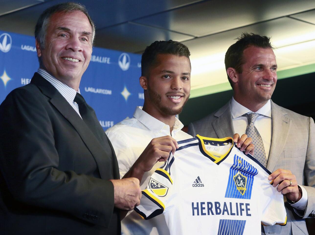 Los Angeles Galaxy coach Bruce Arena, left, and team president Chris Klein, right, pose for a photo with the team's new forward Giovani dos Santosduring an introductory news conference in Carson, Calif., on Tuesday, Aug. 4, 2015. After four years of courting dos Santos, the Galaxy signed the highest-profile Mexican star in their history to a designated player contract, paying a reported $7 million transfer fee. He is expected to make his Major League Soccer debut on Sunday against the Seattle Sounders FC. (AP Photo/Nick Ut)